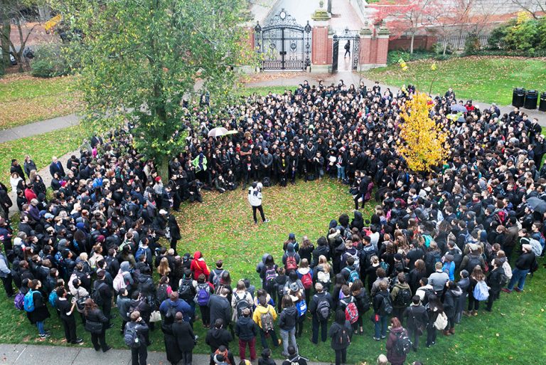 A large group of people stand in a circle around one person holding a megaphone.